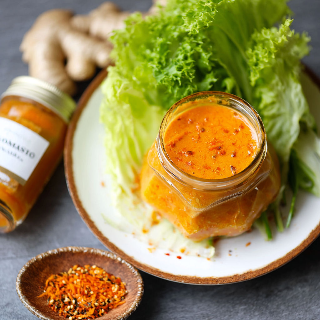 A jar of Japanese carrot ginger dressing sits on a plate with lettuce.