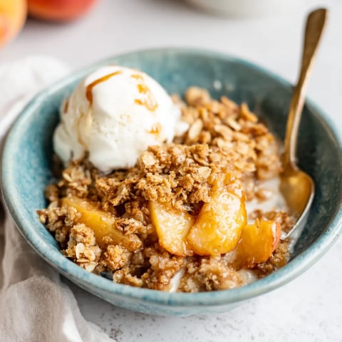 A bowl of peach crisp with a spoon in it.